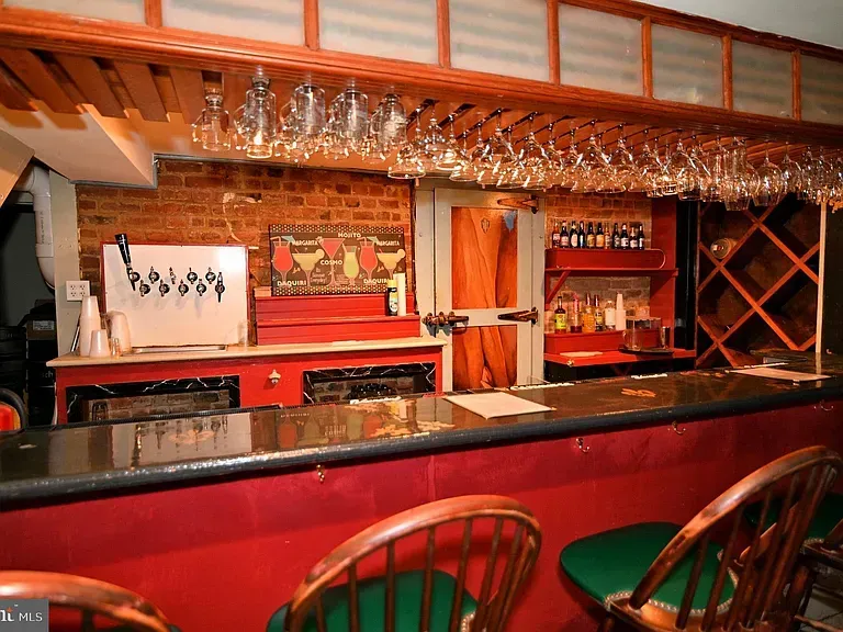 Bar with red counter, green bar stools, brick wall, and hanging glasses.