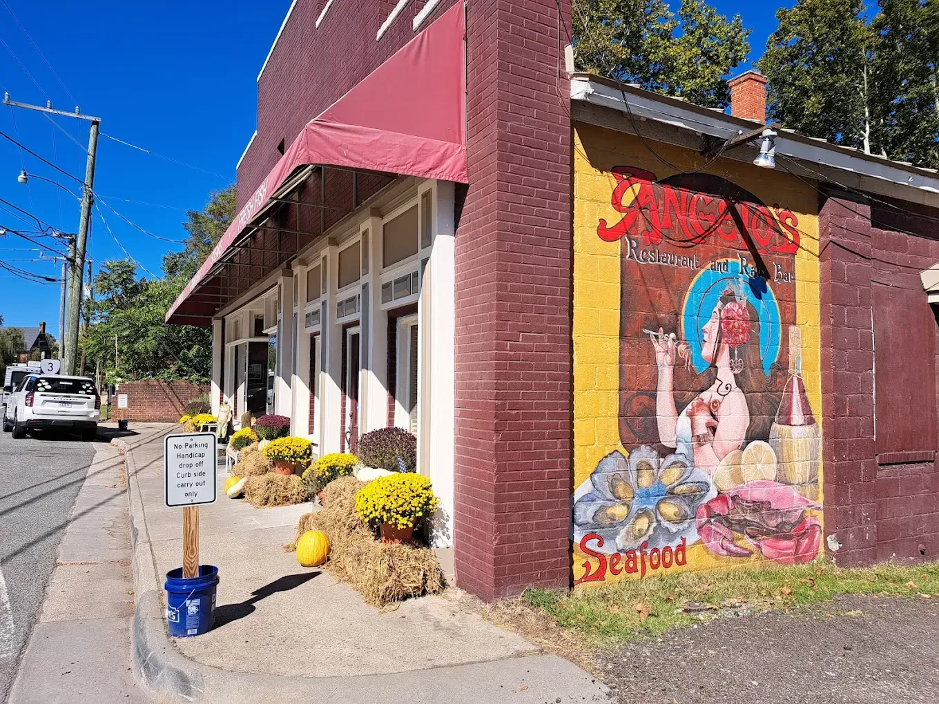 Exterior of a brick restaurant with a red awning and mural of seafood on the side.