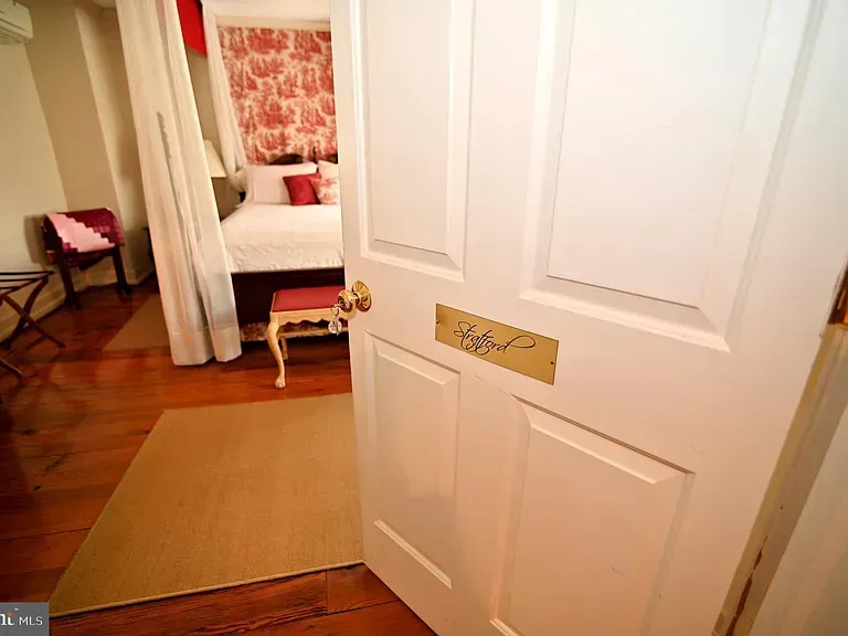 Open white door leads to a bedroom. Bed with red and white decor visible.