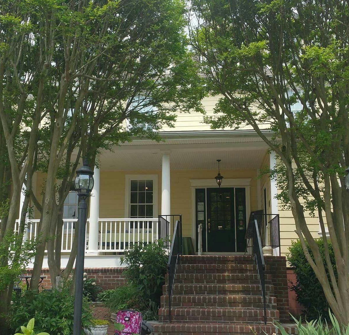 Yellow house with porch, steps, and trees. Dark green door, white columns.