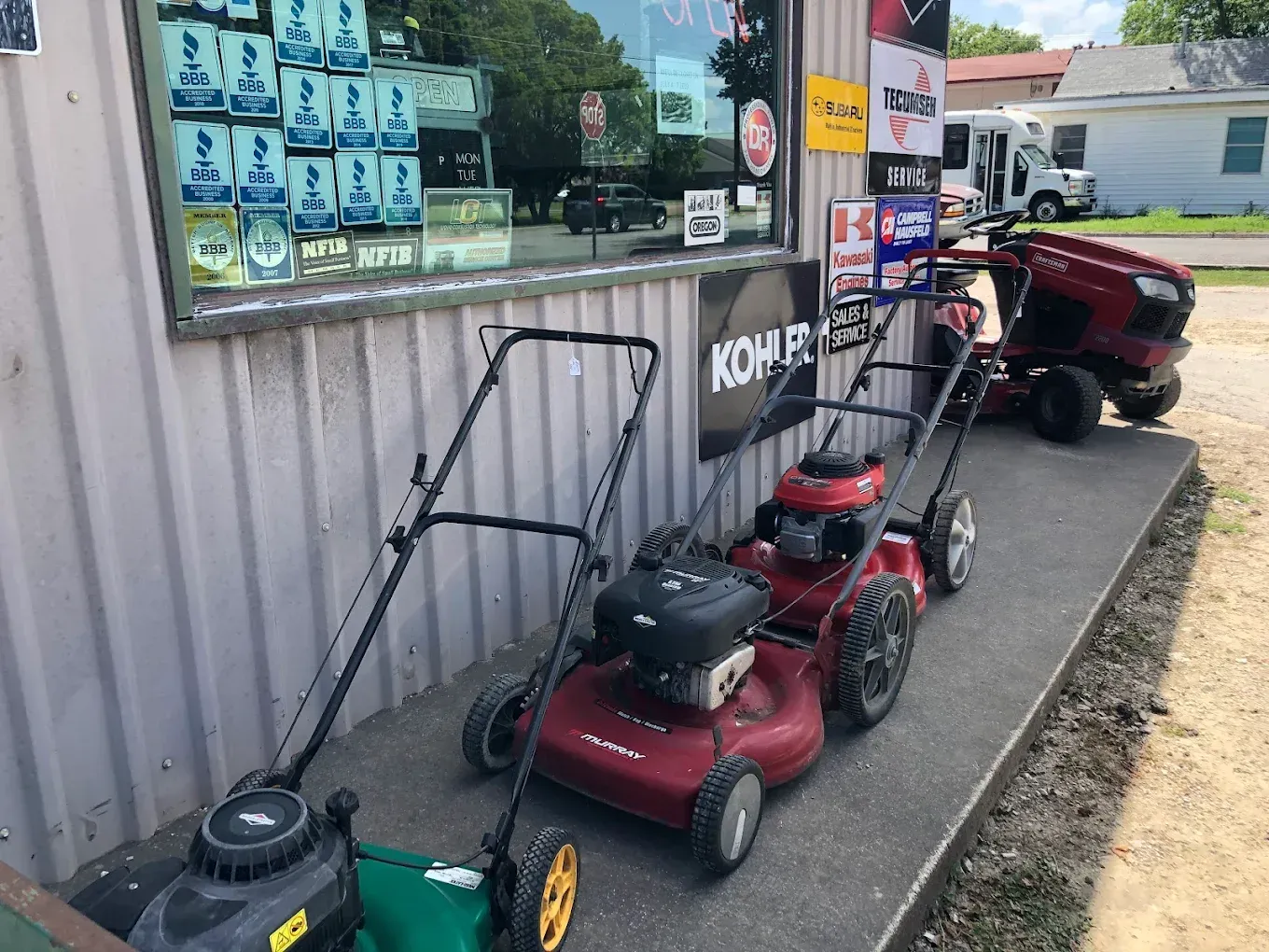 Row of lawnmowers on display outside a store with products in the window.