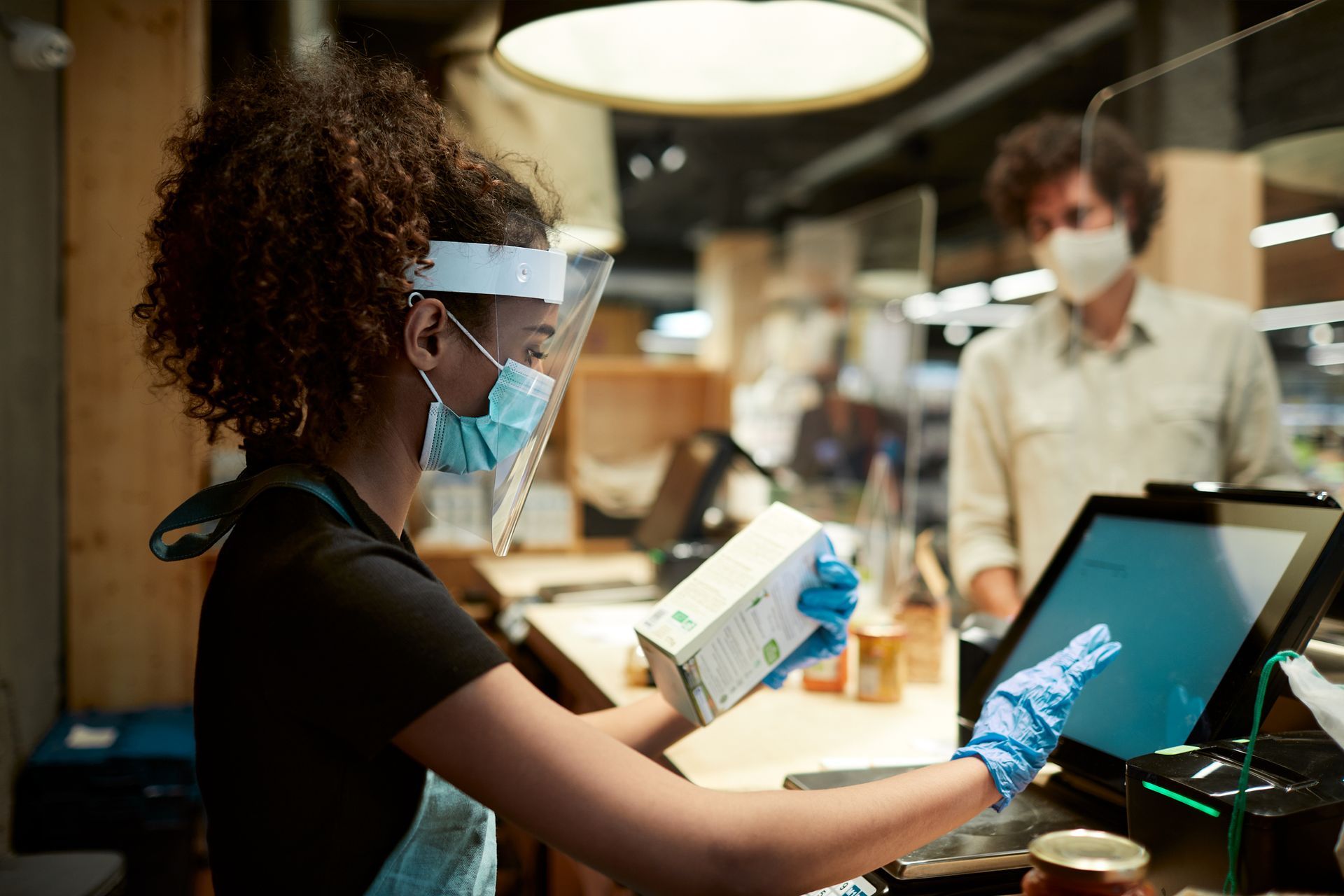 A woman wearing a face shield and gloves is standing at a counter in a store.