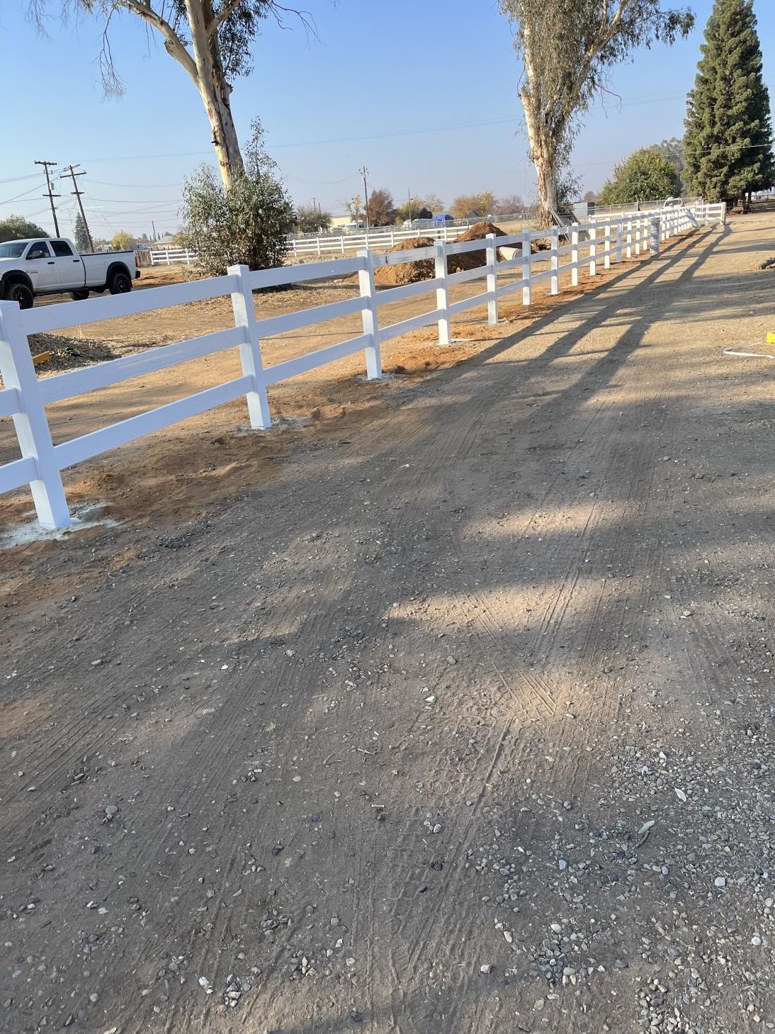 A white fence is along the side of a dirt road.