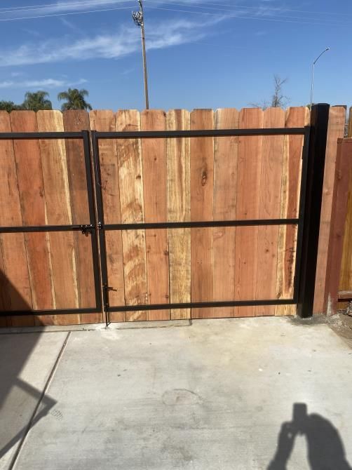 A wooden fence with a black gate is sitting on top of a concrete patio.