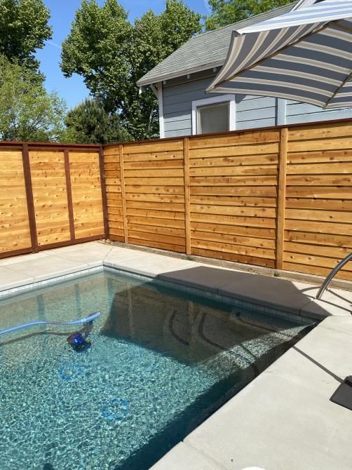 A swimming pool with a wooden fence and a striped umbrella.