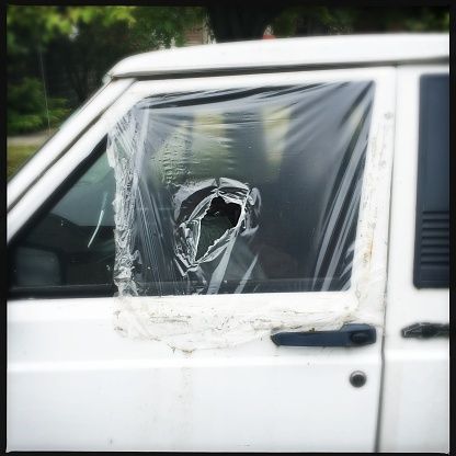 A white car with a broken window covered in plastic