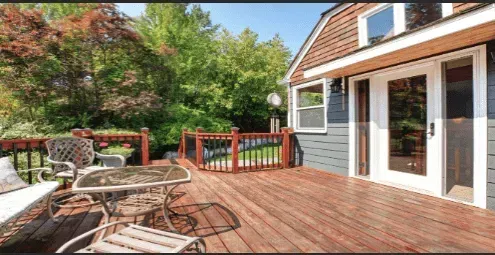 A wooden deck with patio furniture overlooks a lush green yard outside a house with gray siding.