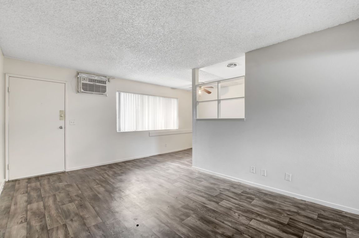 Empty living room with gray walls, wood-look flooring, window AC, and built-in shelving.