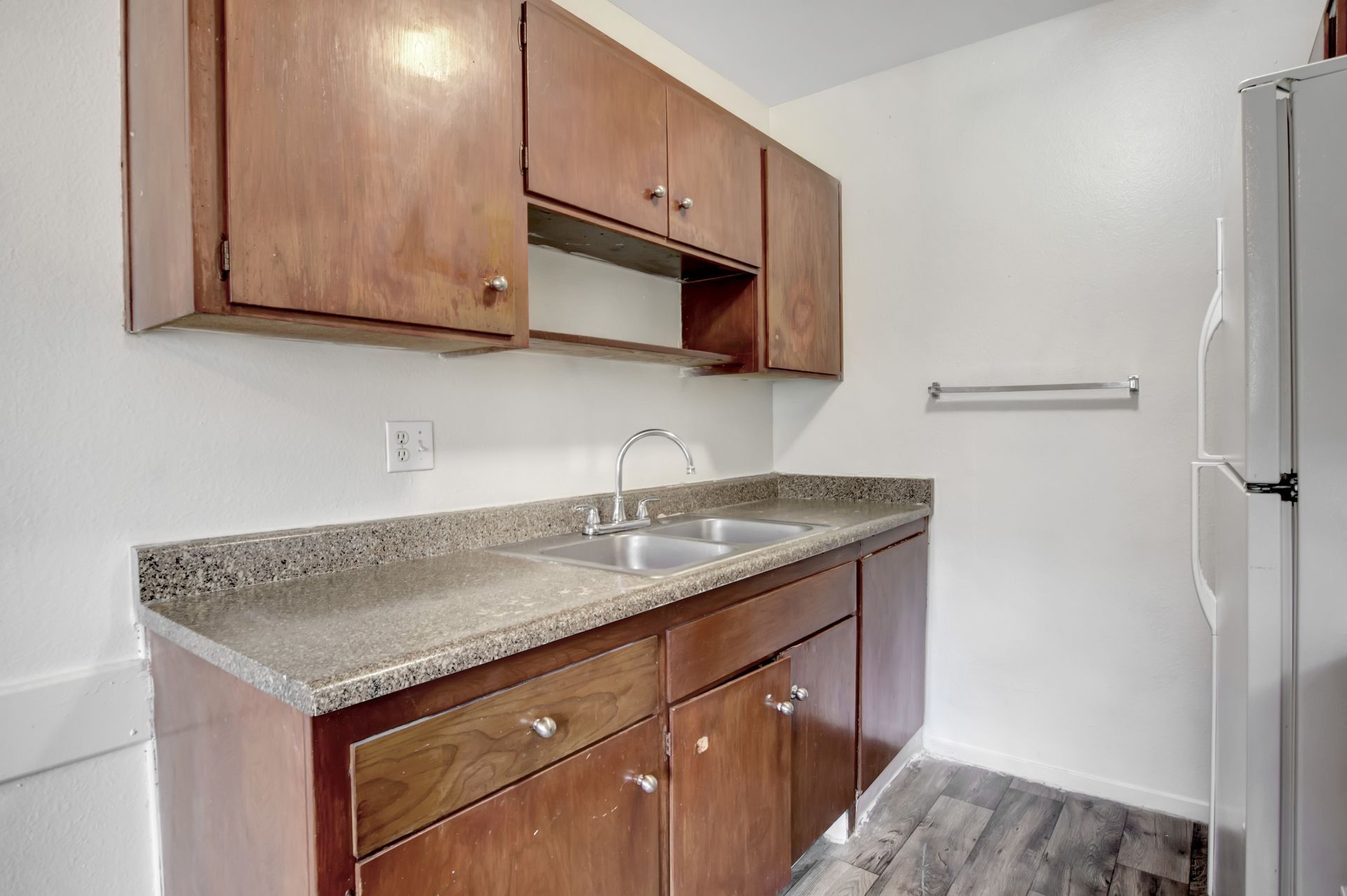 Small kitchenette with wood cabinets, speckled countertop, sink, and refrigerator in a bright room