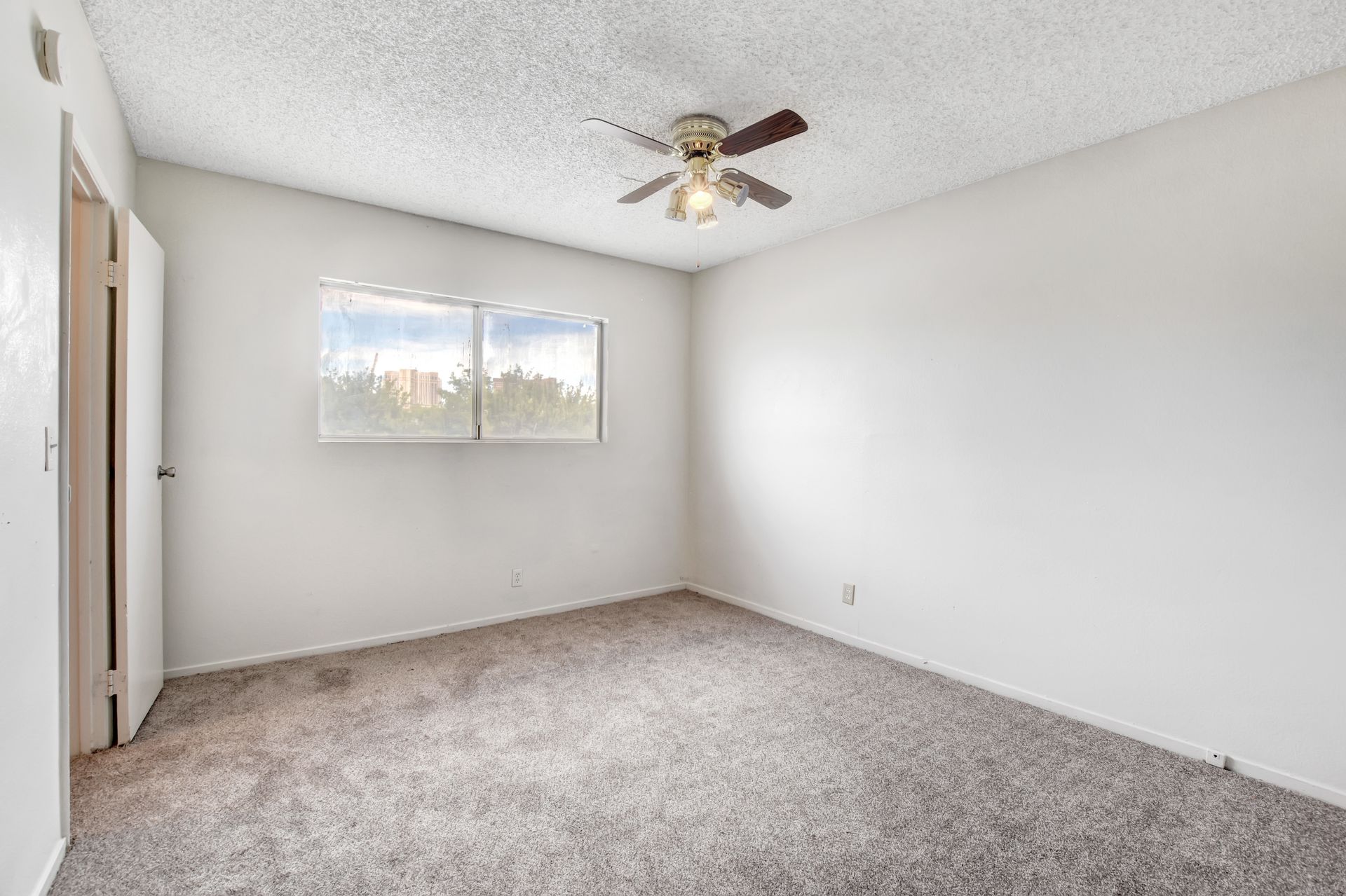 Empty beige bedroom with carpet, ceiling fan, and two windows on the left wall.
