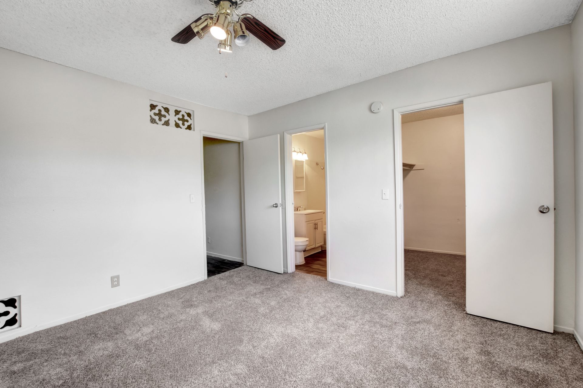 Empty carpeted bedroom with white walls, ceiling fan, and two open closet doors
