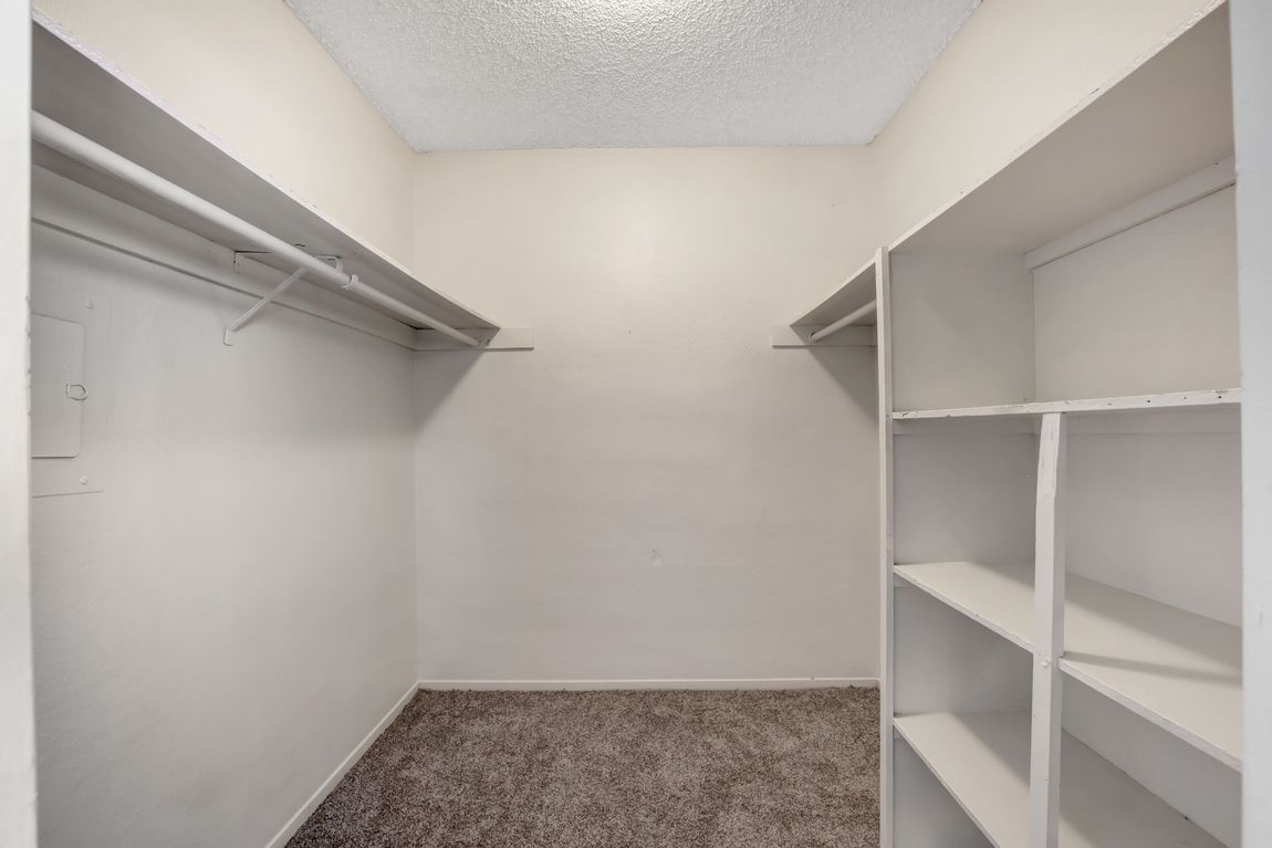Empty walk-in closet with white shelves, hanging rods, and beige carpet.