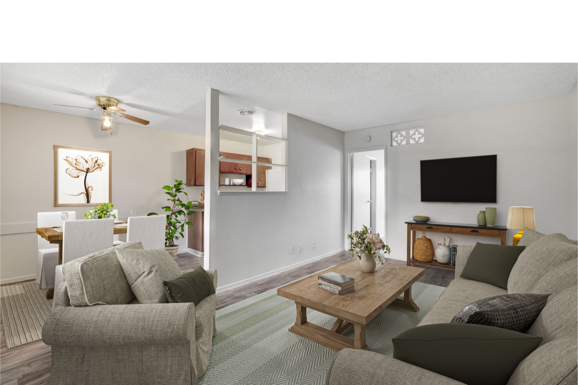 Bright living room with gray sofas, wooden coffee table, wall-mounted TV, and open dining area.