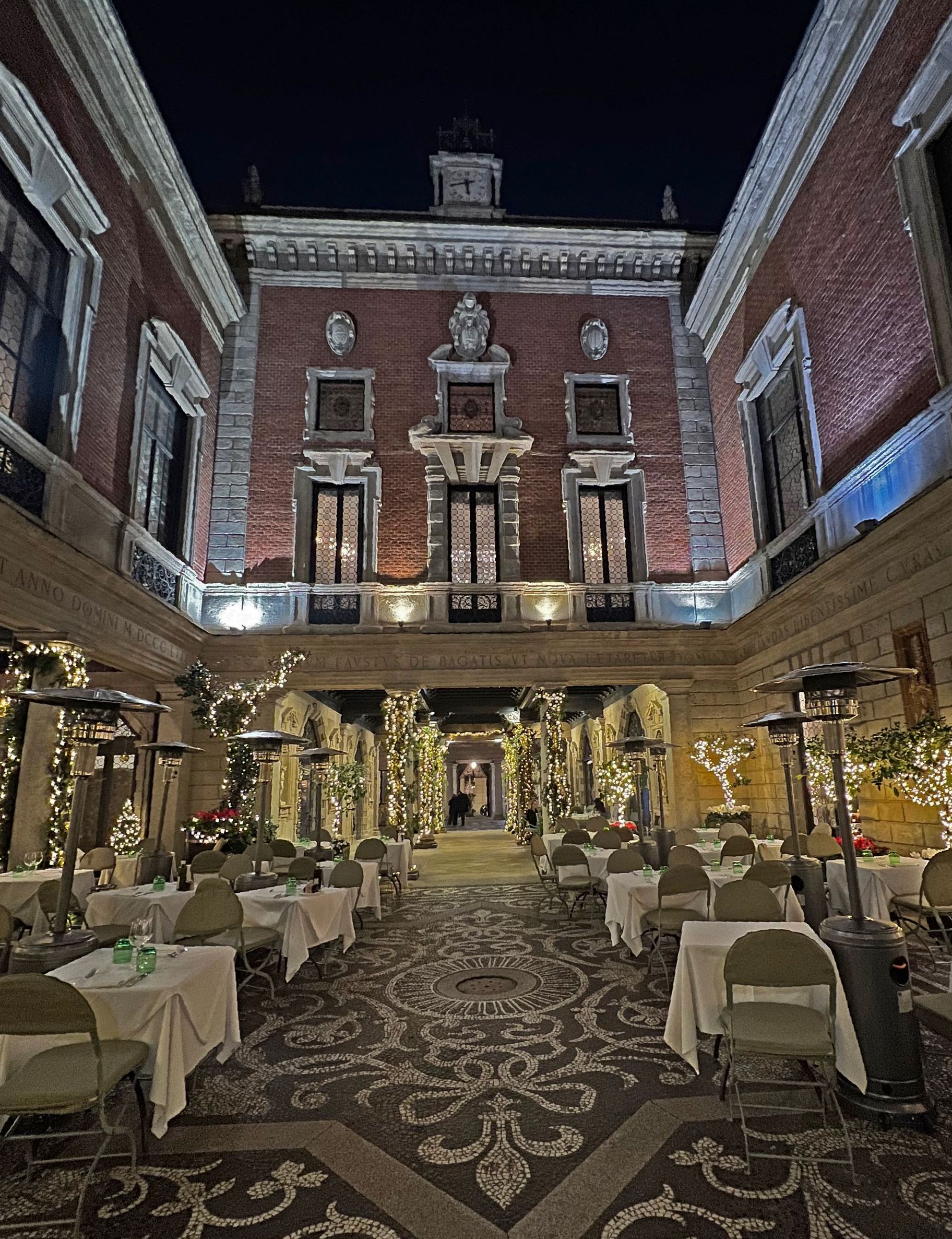 Un grande edificio in mattoni con tavoli e sedie di fronte di notte.