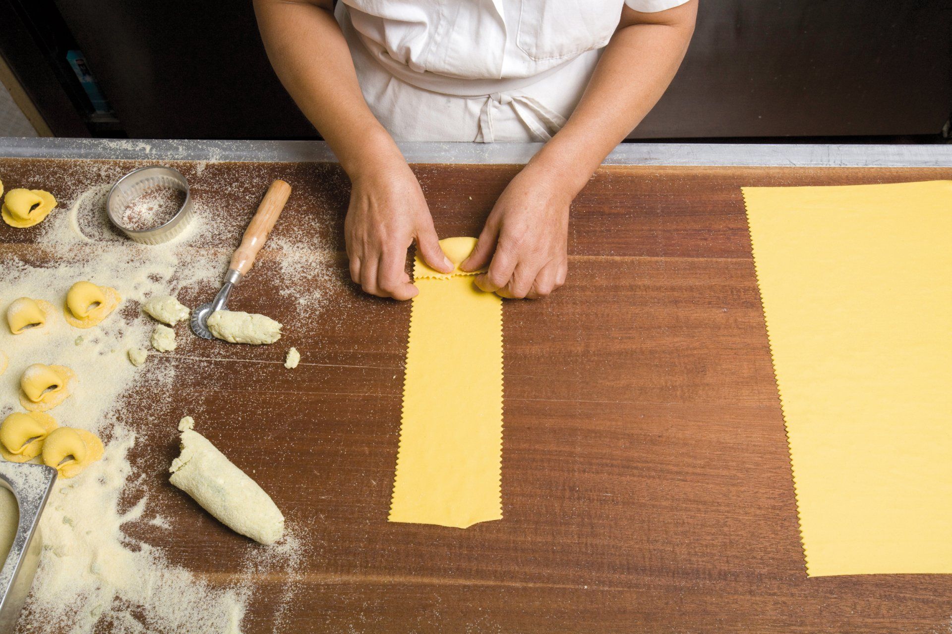 Una persona sta tagliando un pezzo di pasta gialla su un tavolo di legno