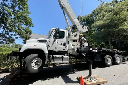 a truck with a crane attached to it is parked on the side of the road .
