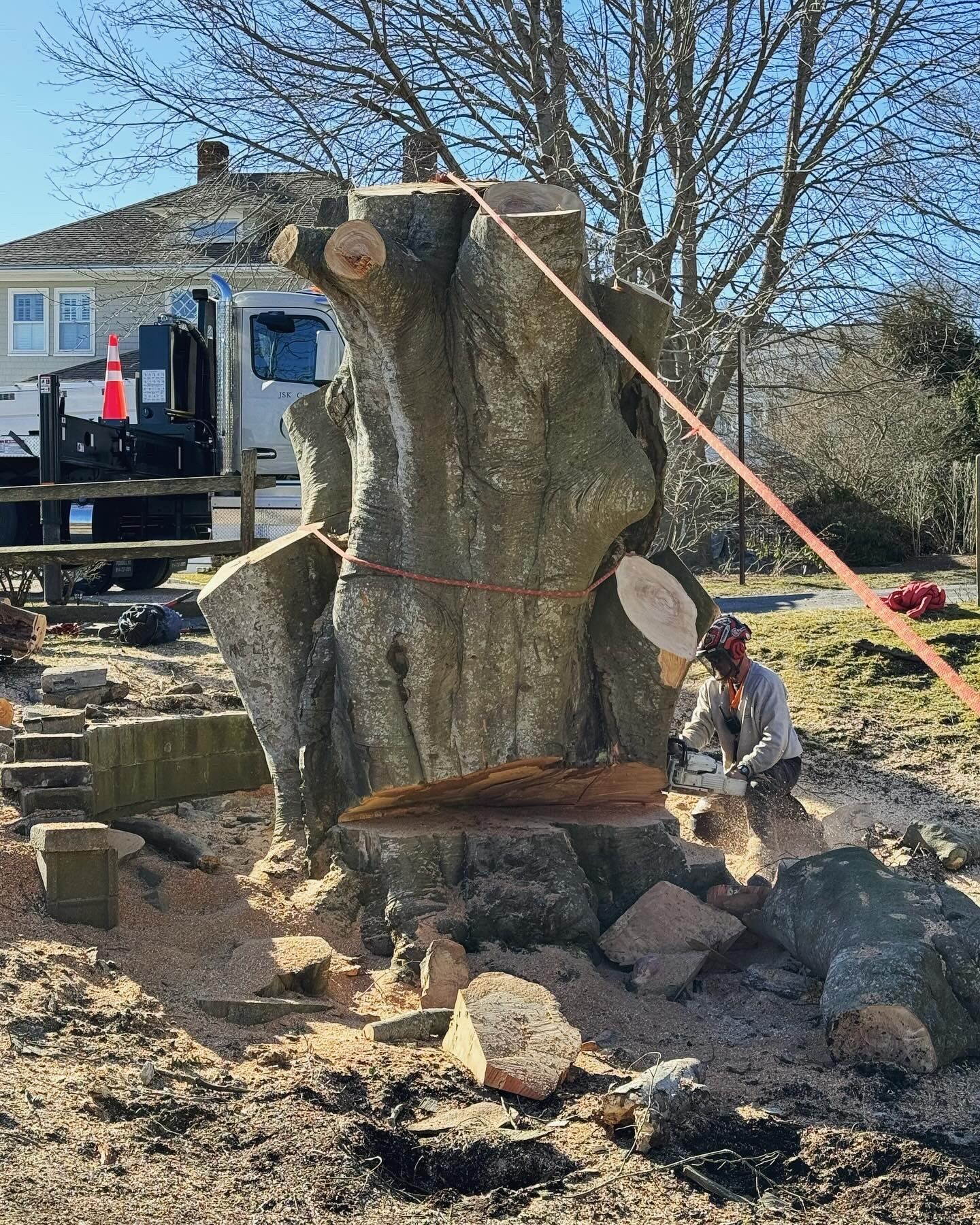 A man is cutting a large tree stump with a chainsaw.