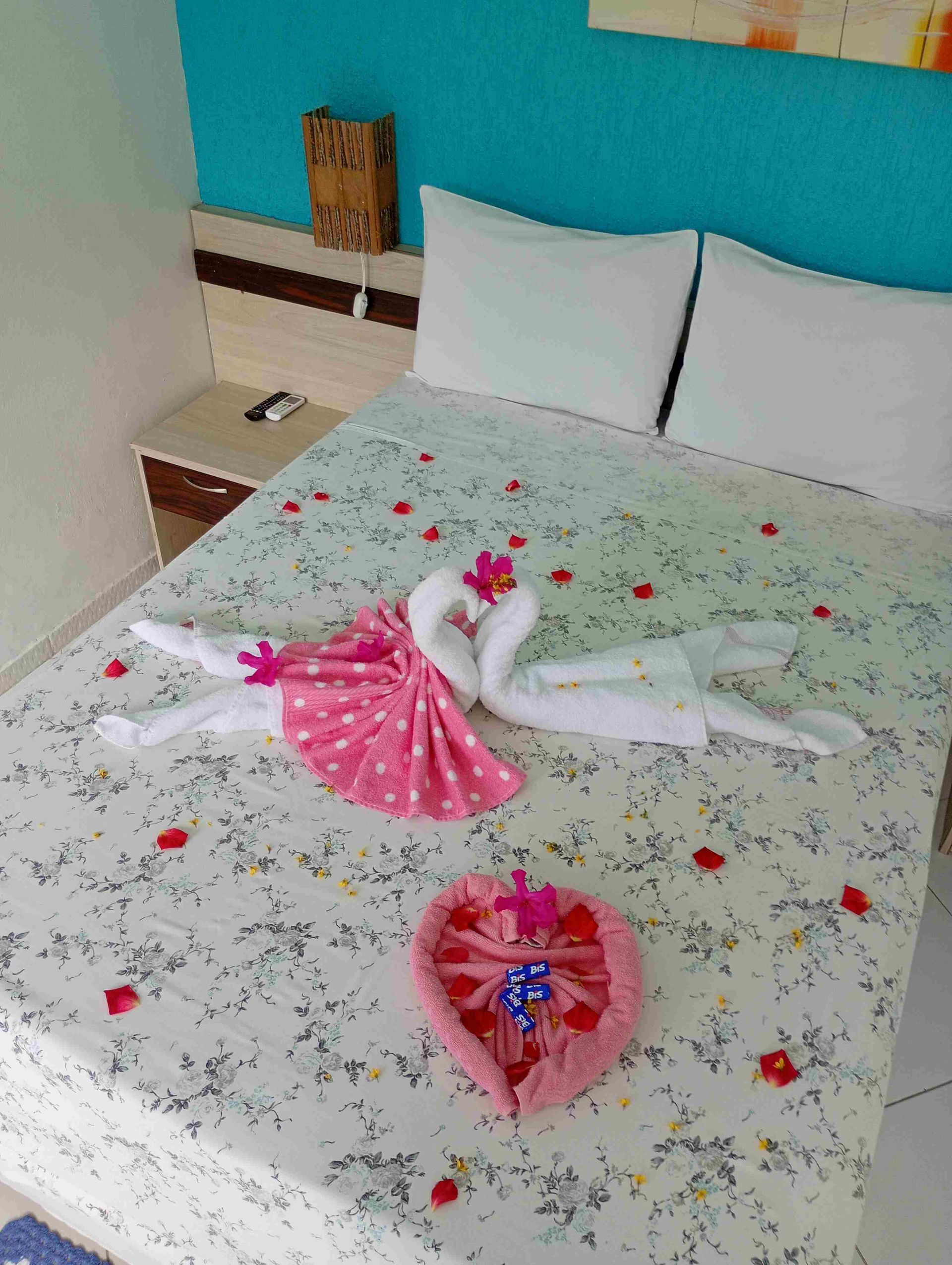 Cama decorada com cisnes de toalha, um coração e pétalas de rosa, em um quarto.