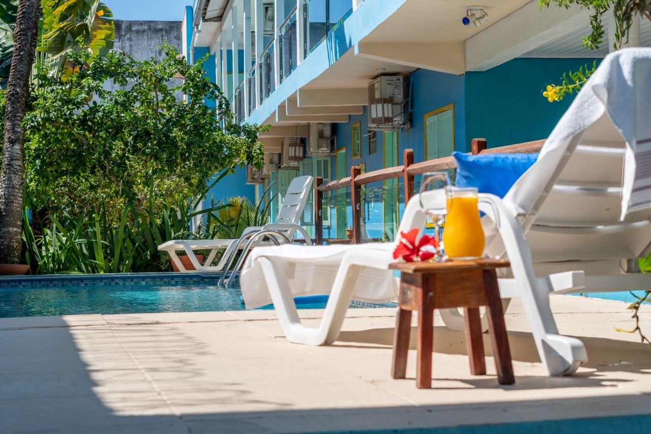 Cena à beira da piscina com espreguiçadeira, suco, hibisco e prédio azul.