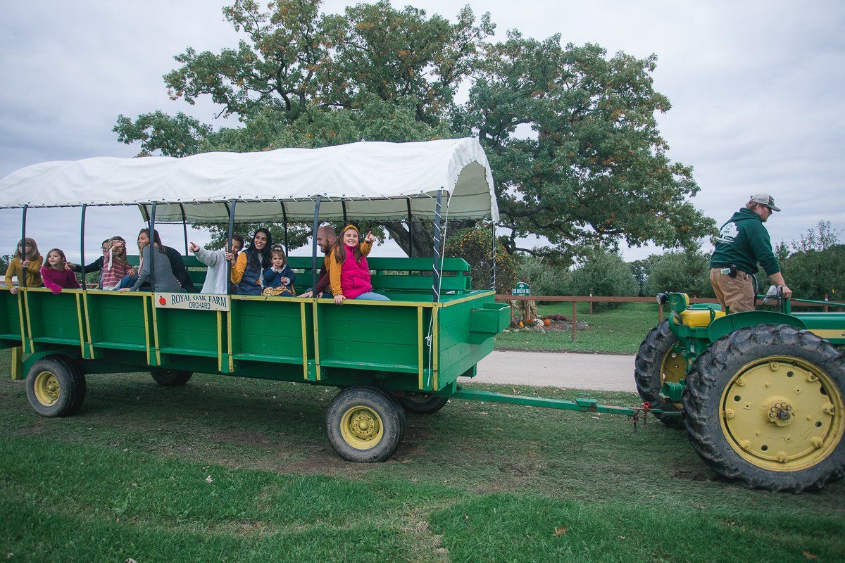 A group of people are riding on a green wagon pulled by a john deere tractor