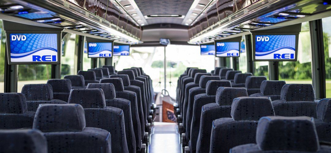 The inside of a bus with a lot of seats and televisions on the ceiling.