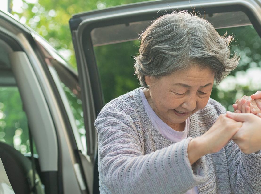 An elderly woman is getting out of a car and holding another woman 's hand.