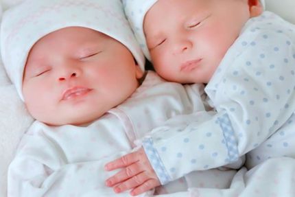 Two newborn babies are sleeping next to each other on a bed.