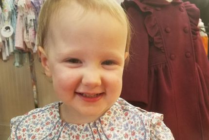 A little girl in a floral dress is smiling for the camera.