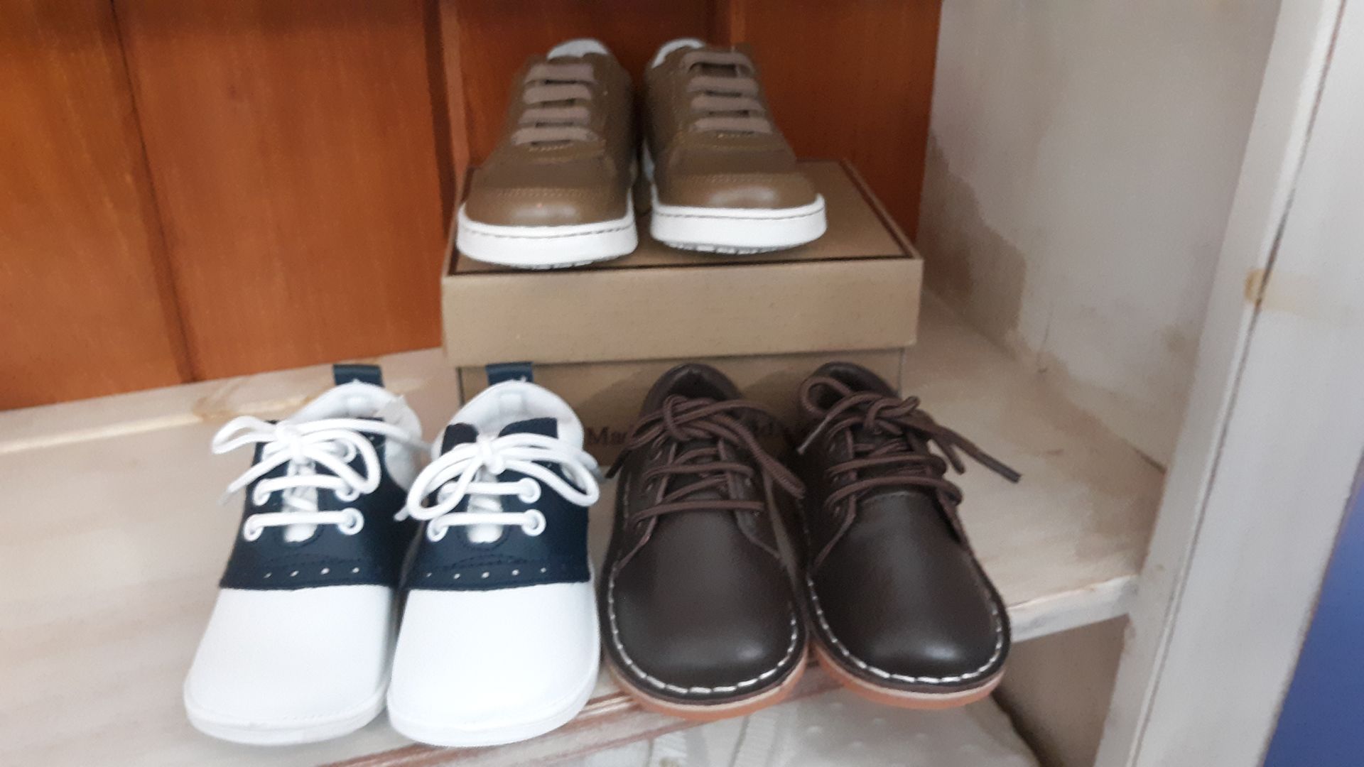 Three pairs of shoes are sitting on a wooden shelf.