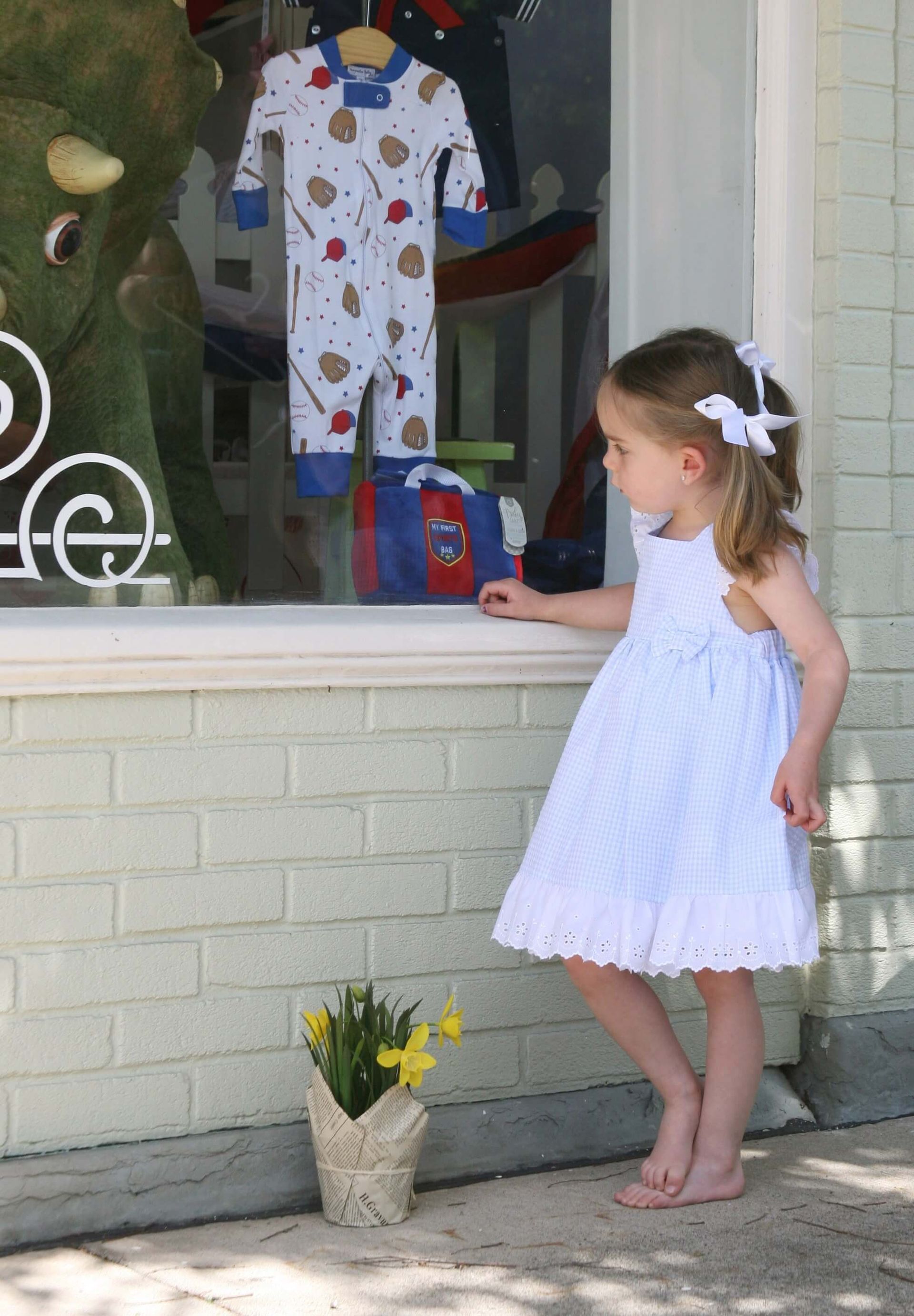 A little girl in a white dress stands in front of a store window