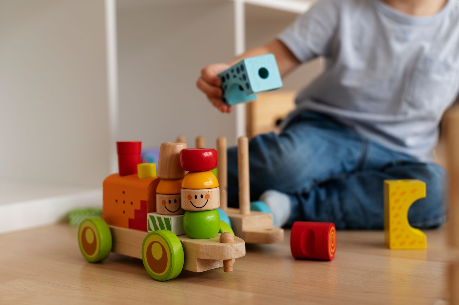A child is playing with a wooden toy train on the floor.