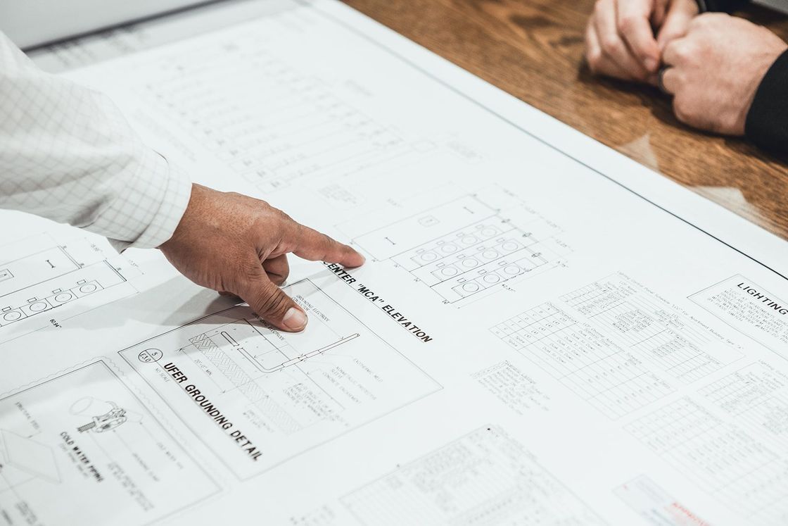 a person is pointing at a blueprint on a table .
