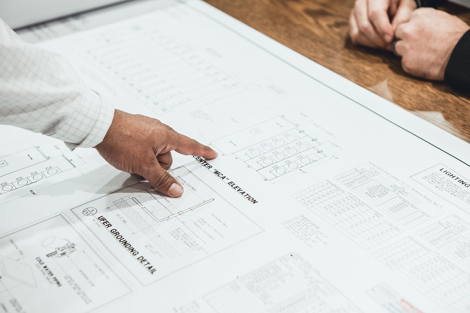 A person is pointing at a blueprint on a table.