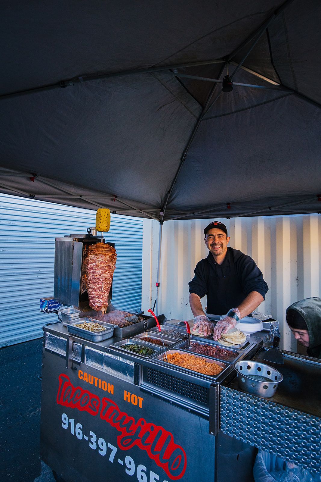 a man is standing behind a food stand under a tent .