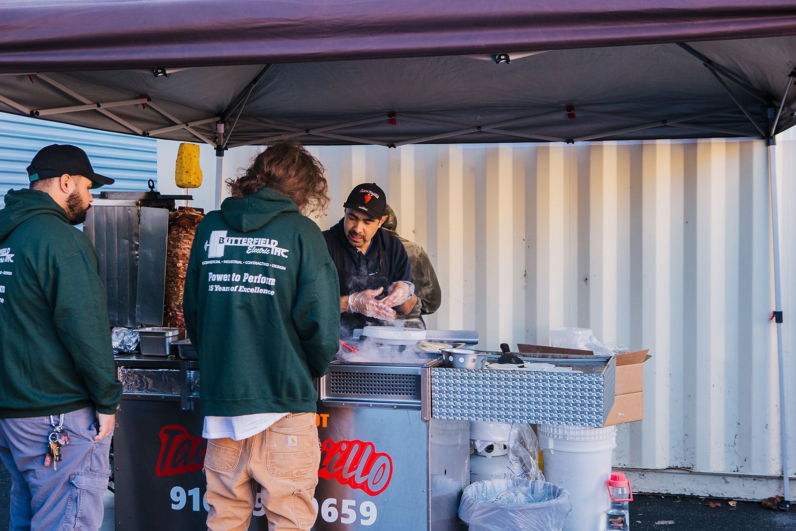 a group of men are standing around a food stand under a tent .