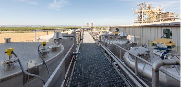A walkway leading to a factory with a lot of tanks and pipes.