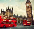 Two red double decker buses are driving in front of big ben in london.