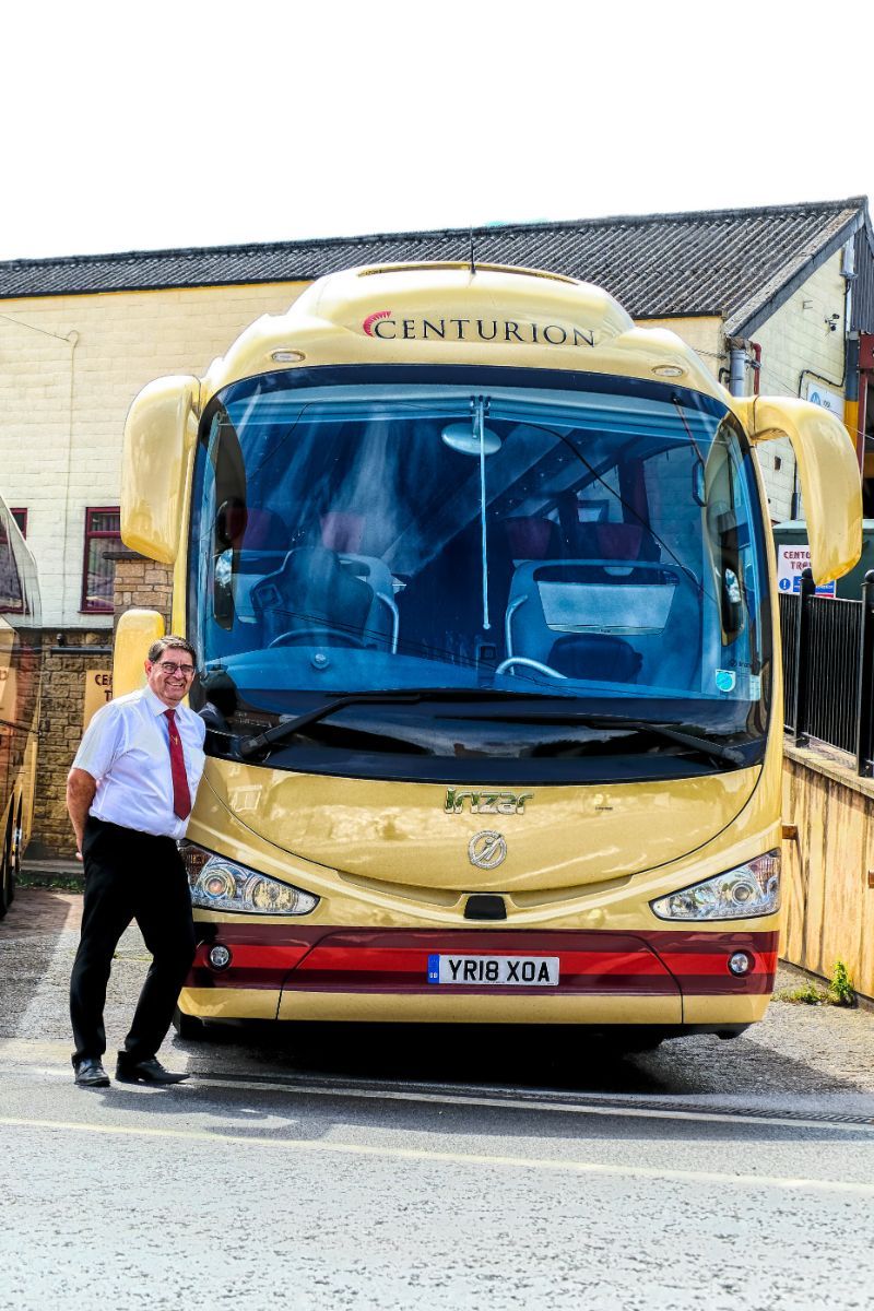 A man is standing in front of a yellow bus.