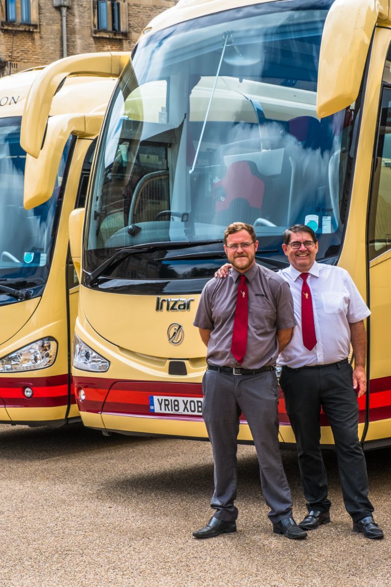 Two men are standing in front of a row of buses.