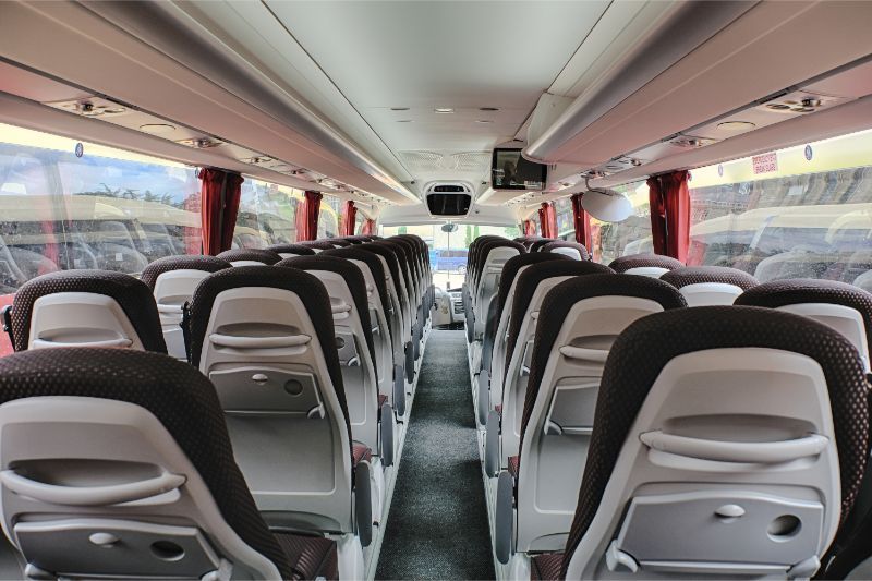 The inside of a bus with rows of seats and a television on the ceiling.