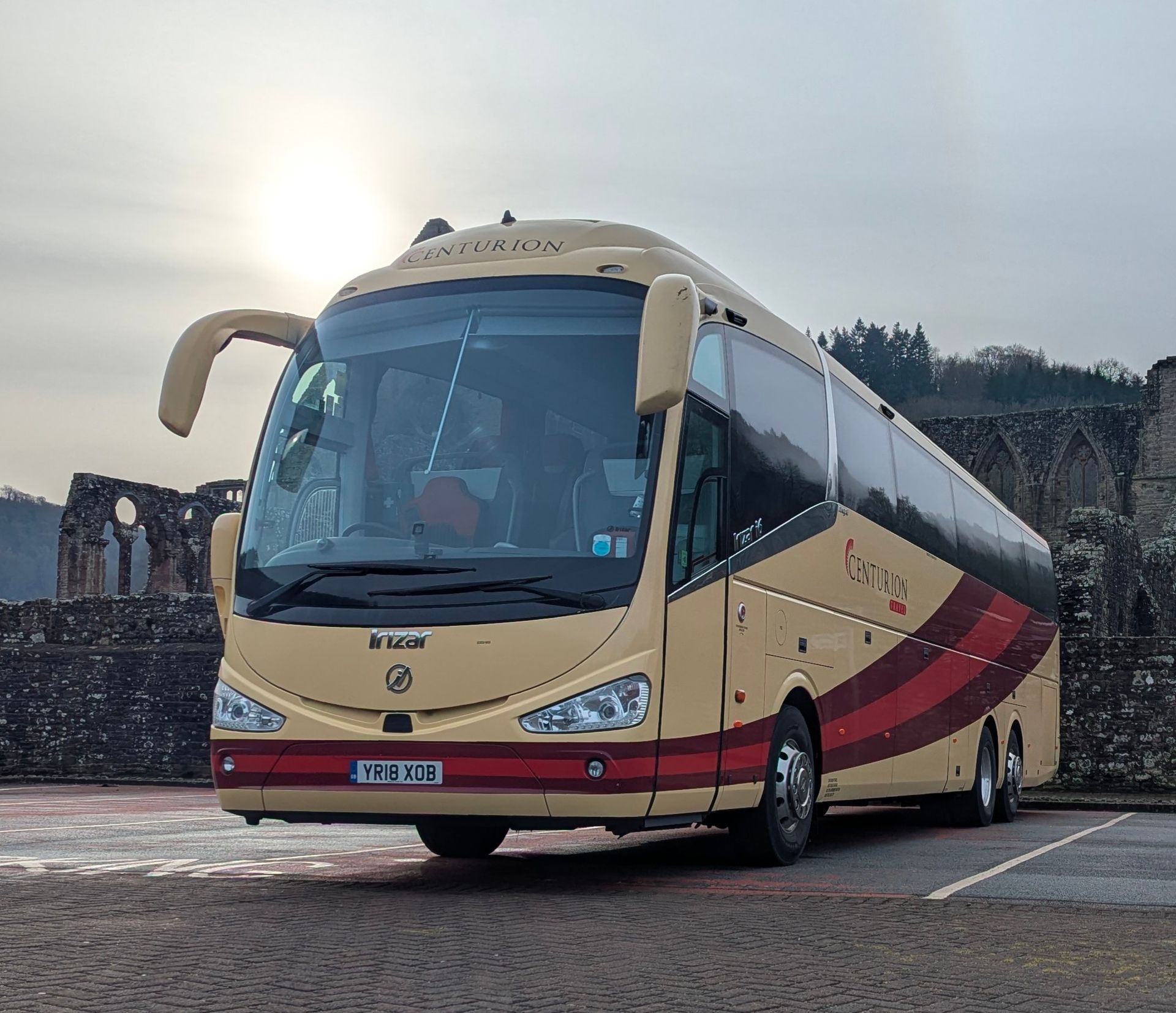 A large bus is parked in front of a stone wall.