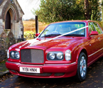 A red wedding car is parked in front of a church.