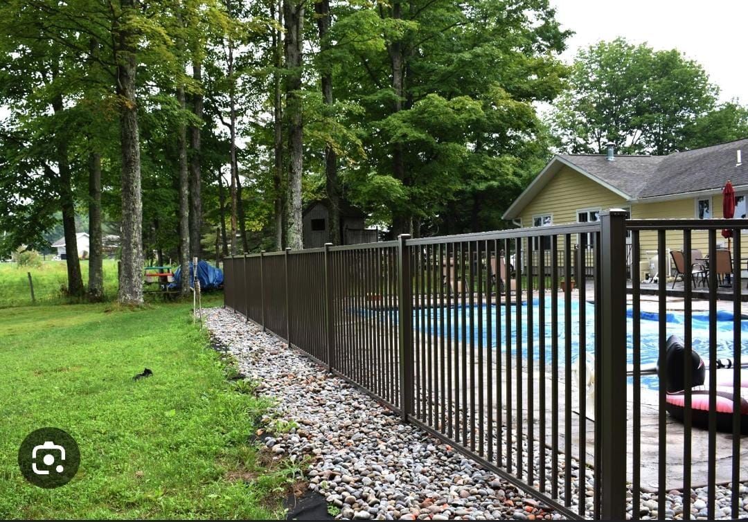 A metal fence surrounds a swimming pool with a house in the background.