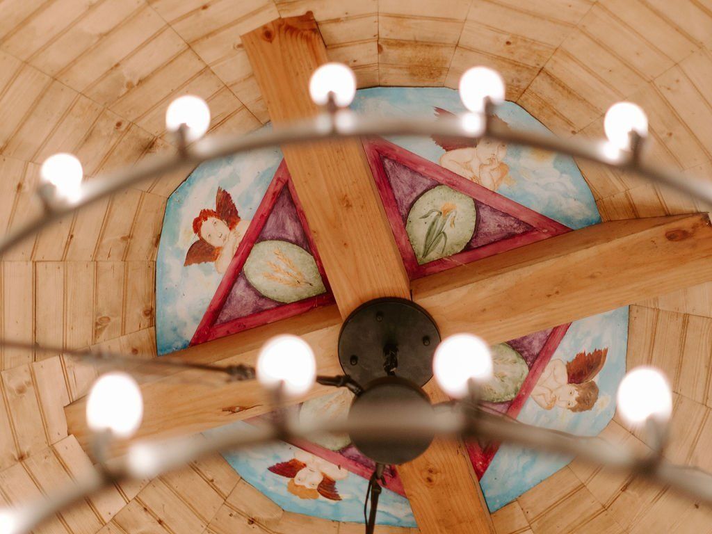 Chandelier with glowing lights, wooden beams, and painted ceiling decoration.