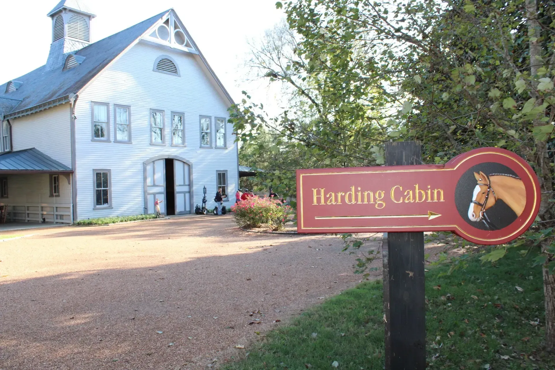 Sign for Harding Cabin with horse graphic, gravel drive, white barn in background.