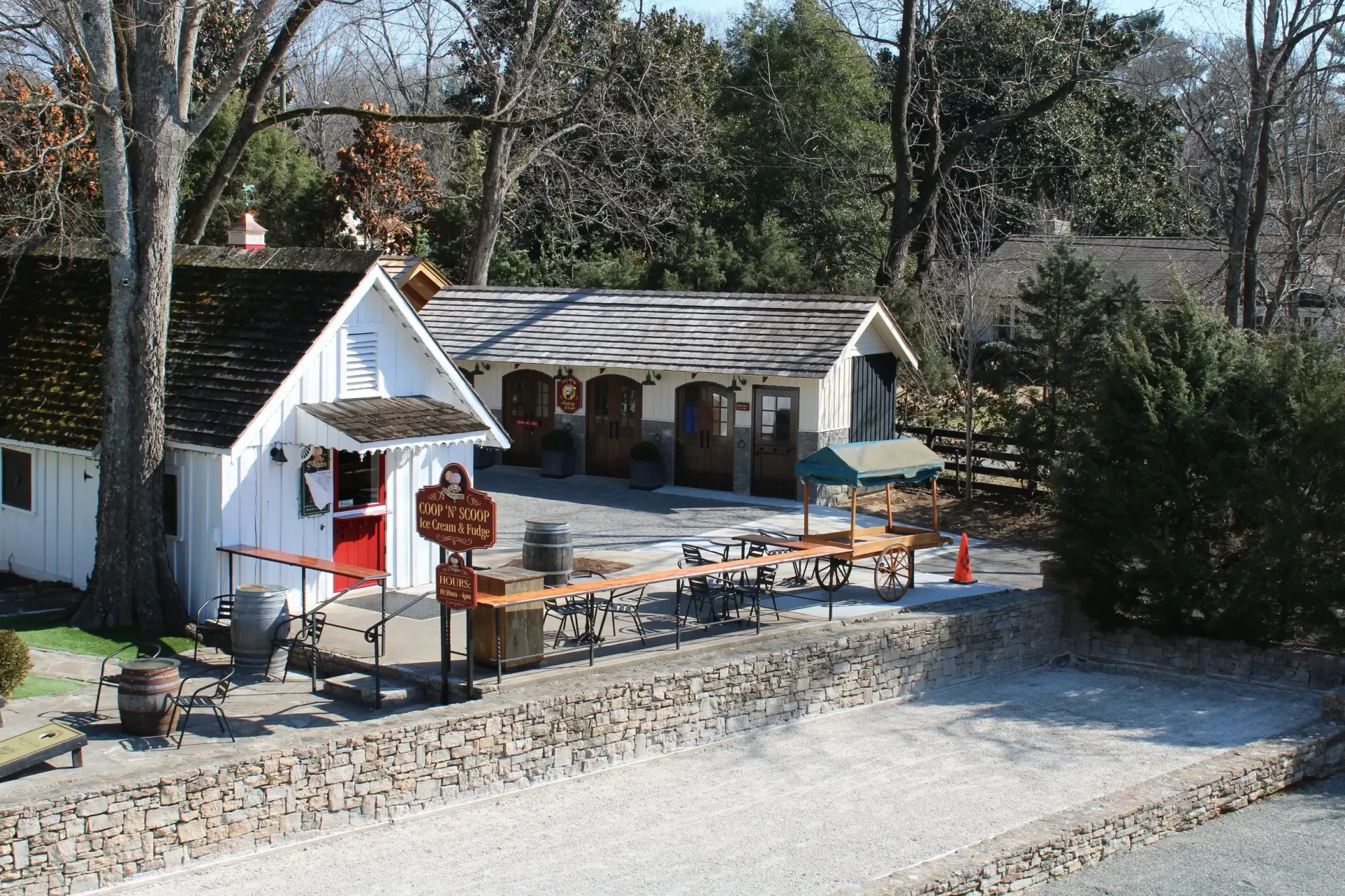 White buildings with a red door and picnic tables set up on a gravel lot; trees in the background.