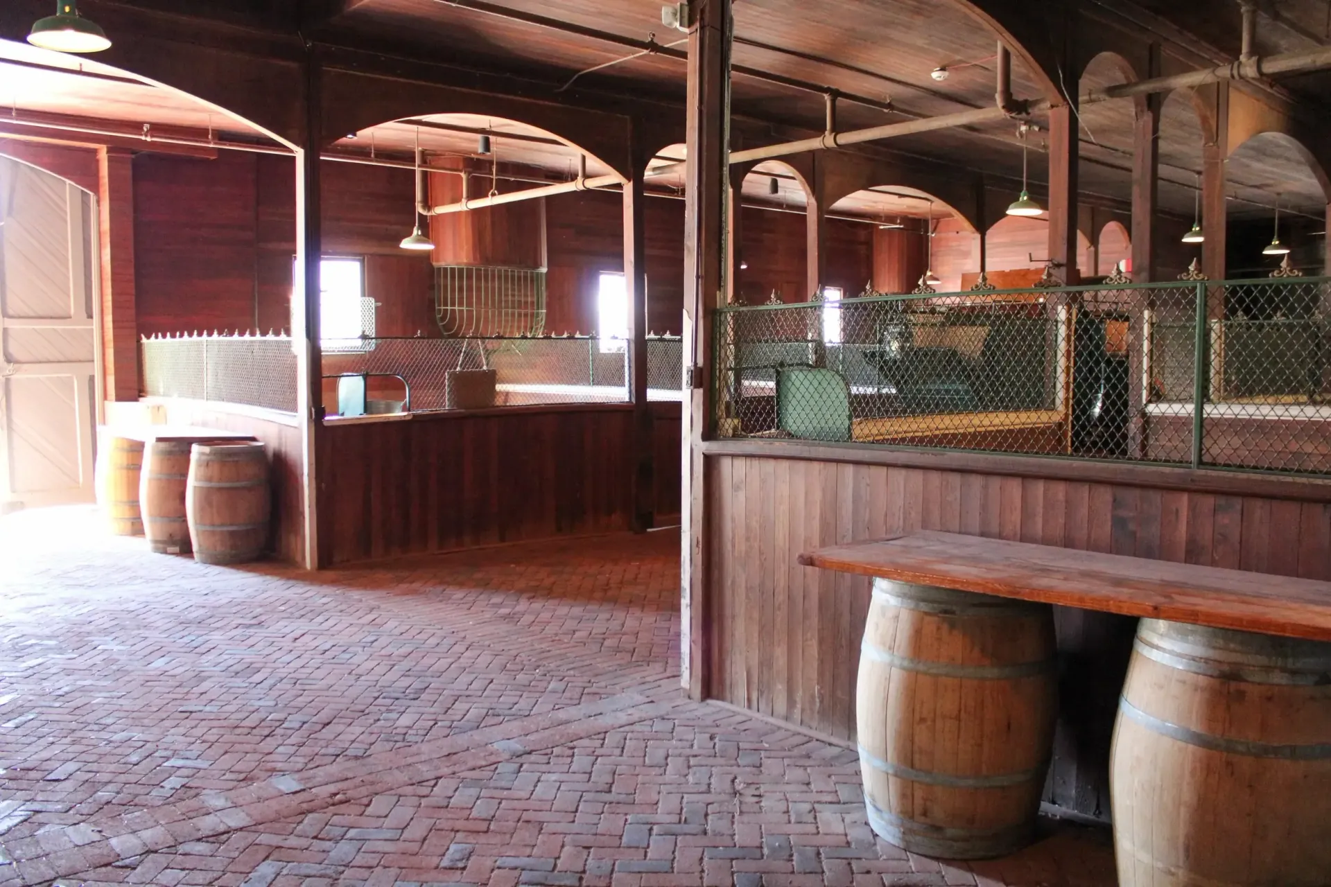 Interior of a rustic barn with wooden stalls, brick floor, and barrels.