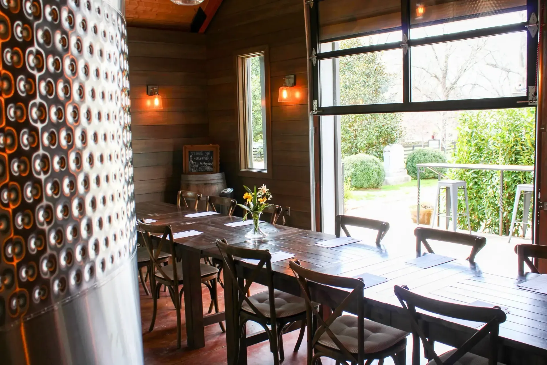 Dining room with long table, chairs, open door to garden. Rustic wood and metal details.
