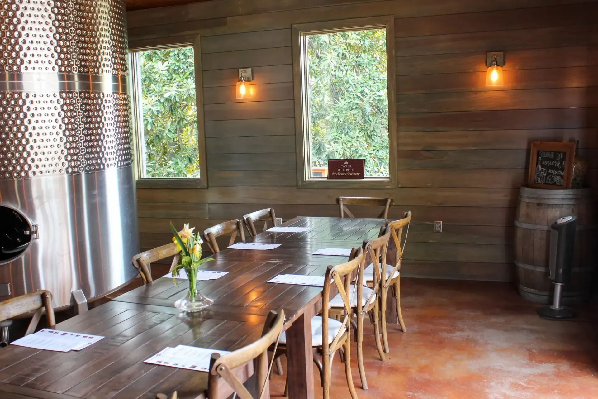 Wine tasting room with a long wooden table, chairs, and stainless steel tank.