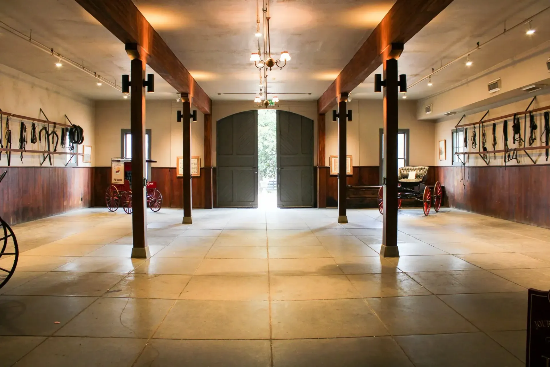 Inside of a stable with wooden beams, open doors and horse tack displayed.